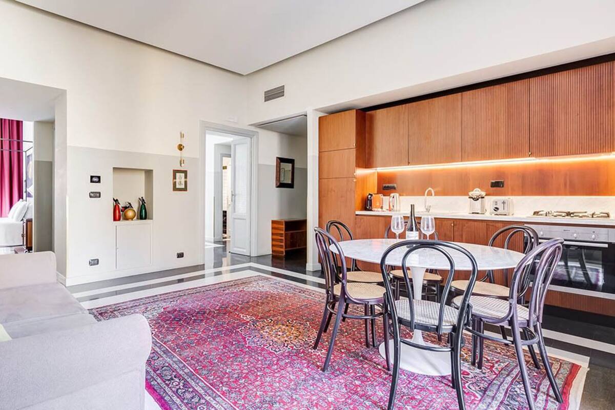 Una sala de estar moderna con un sofá, una mesa de comedor con sillas y una cocina con armarios de madera y una encimera.