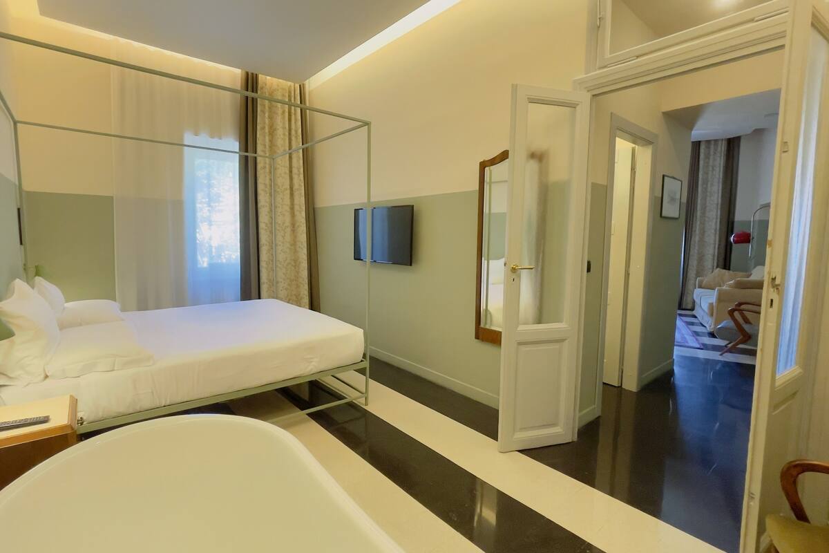 Habitación de hotel moderna con cama, televisor, espejo y baño visible a través de una puerta abierta.