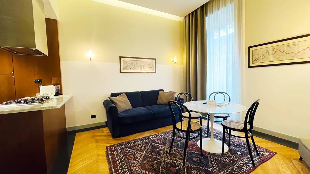 A compact living space with a kitchenette, a dark blue sofa, a dining table with chairs, and a patterned rug.