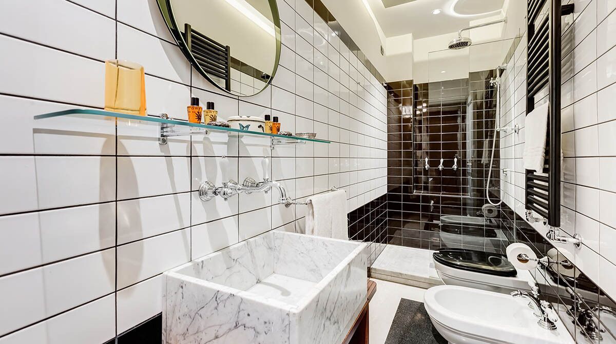 A modern bathroom with a marble sink, a glass shelf with toiletries, a separate toilet, and a shower area.