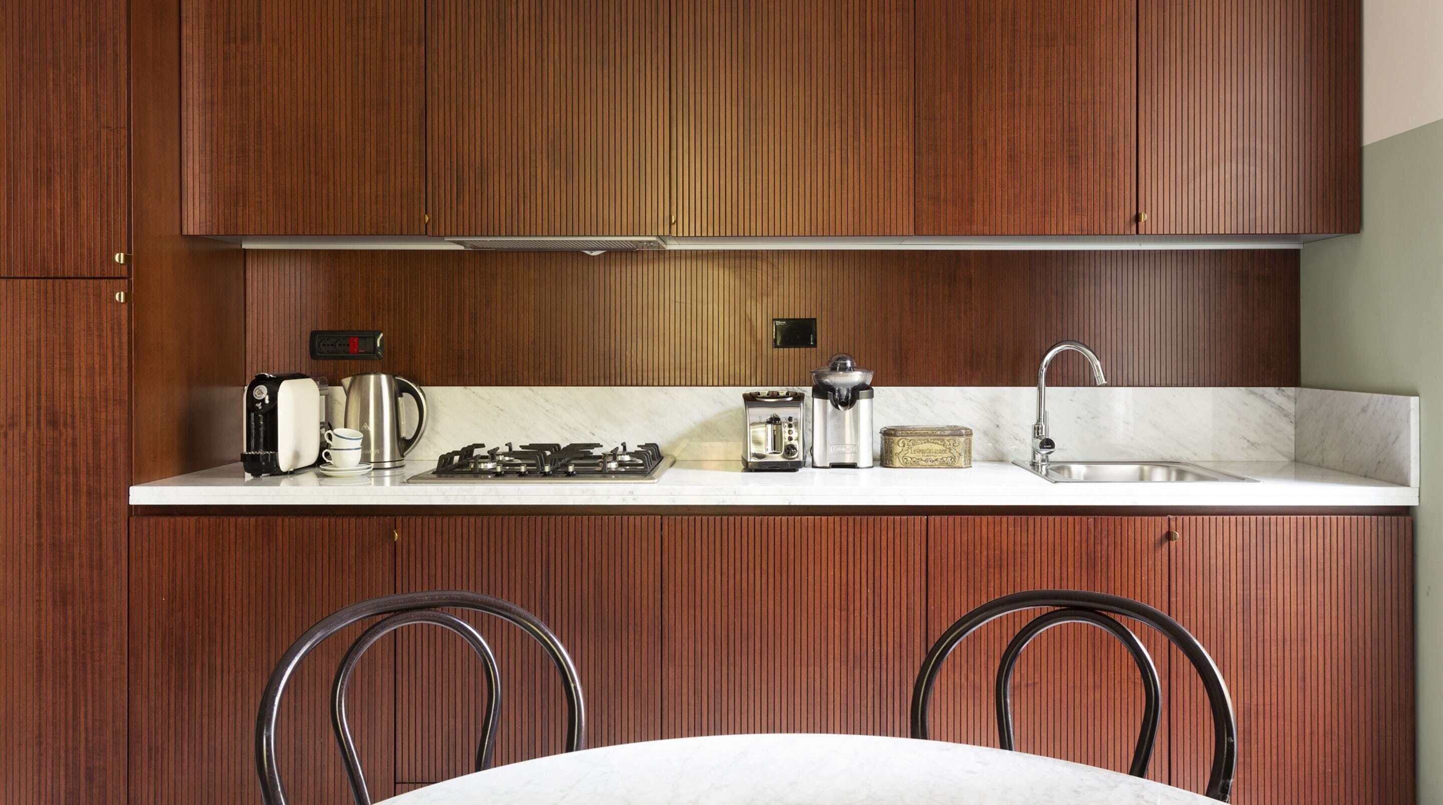 A kitchen with wooden cabinets, a white countertop, a gas stove, a coffee maker, a toaster, a kettle, and a sink.