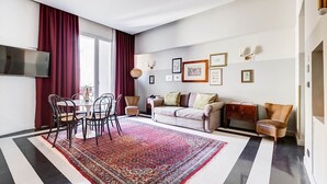 Een moderne woonkamer met een eethoek, een zithoek, een aan de muur bevestigde televisie en wanddecoratie.
