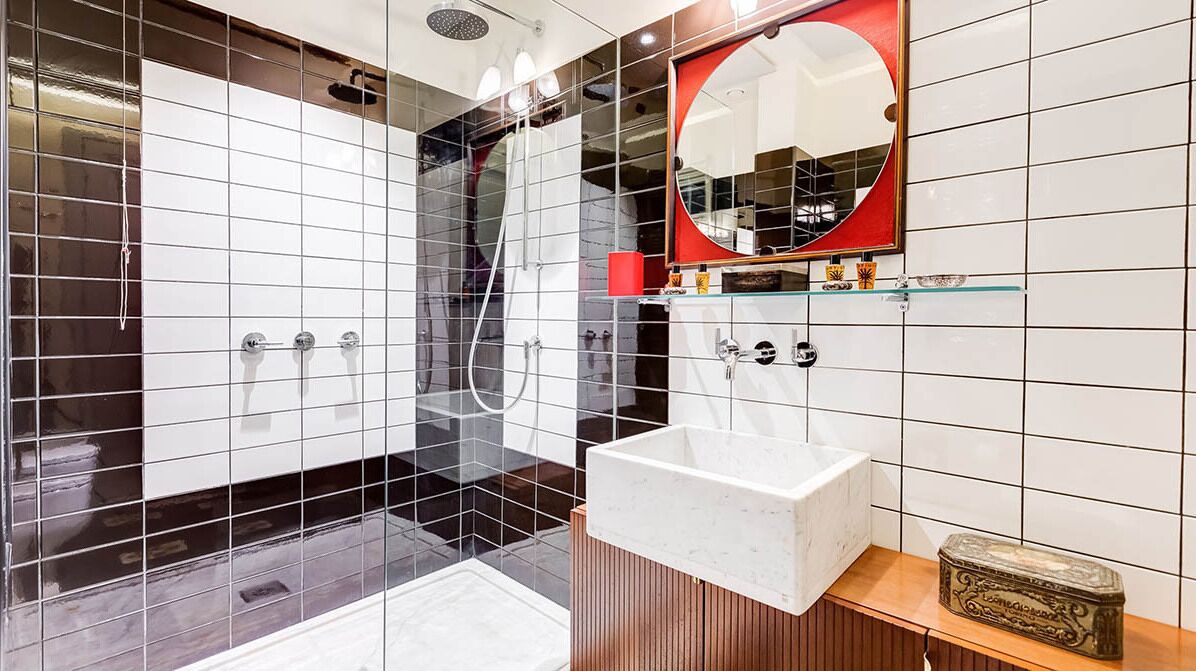 Un baño moderno con ducha acristalada, un lavabo blanco y un espejo con marco rojo.
