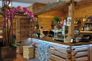 Angolo bar rustico con pareti in legno, un bancone in pietra e diverse bottiglie e bicchieri.