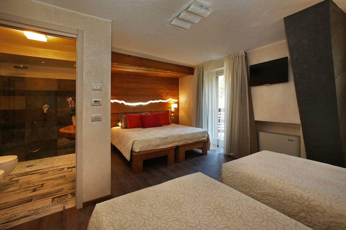 Une chambre d’hôtel avec un lit en bois, une salle de bain séparée, un téléviseur à écran plat et un petit bureau.