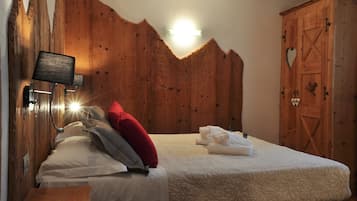 A bedroom with a wooden headboard, a bedside table with a lamp, a bed with white bedding and a red pillow, and a wooden wardrobe with a heart-shaped cutout.