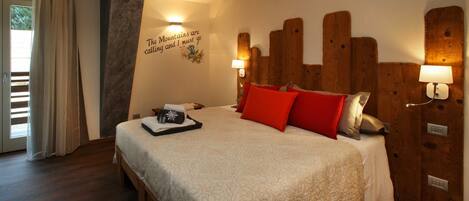 A neatly made bed with a floral bedspread, red and grey pillows, and a tray with a glass and a small item.