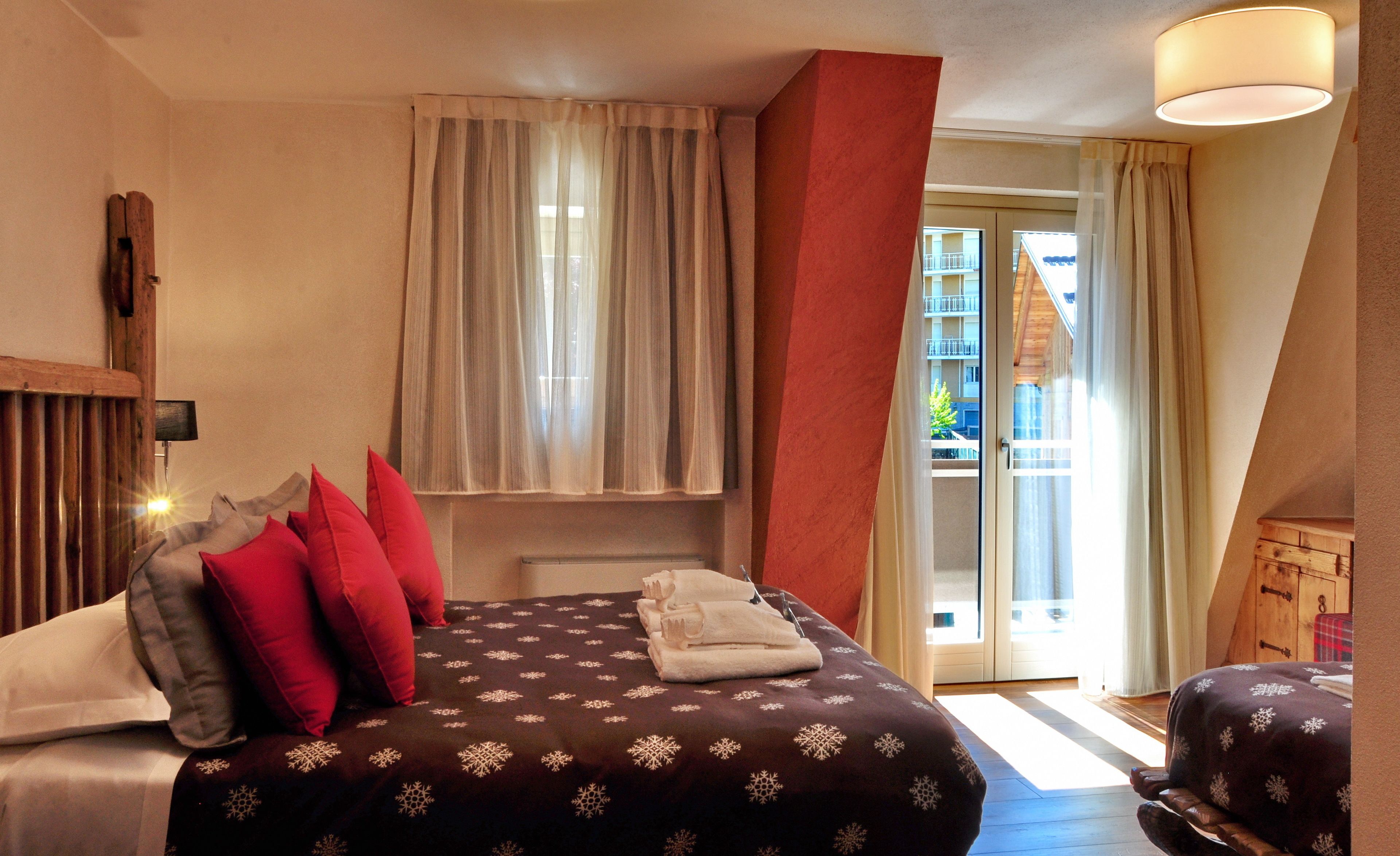 Ein Hotelzimmer mit einem Bett, Kissen, einem Fenster mit Vorhängen, einem Holz-Kopfbrett und Blick auf den Außenbalkon.