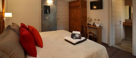 Habitación de hotel con cama, armario de madera, escritorio con silla, televisión y baño visible a través de una puerta abierta.
