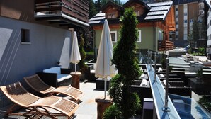 Terraza en la azotea con sillones de madera, sombrillas y una piscina.