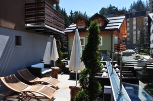 Una terrazza sul tetto con poltrone da relax in legno, ombrelloni e una piscina.