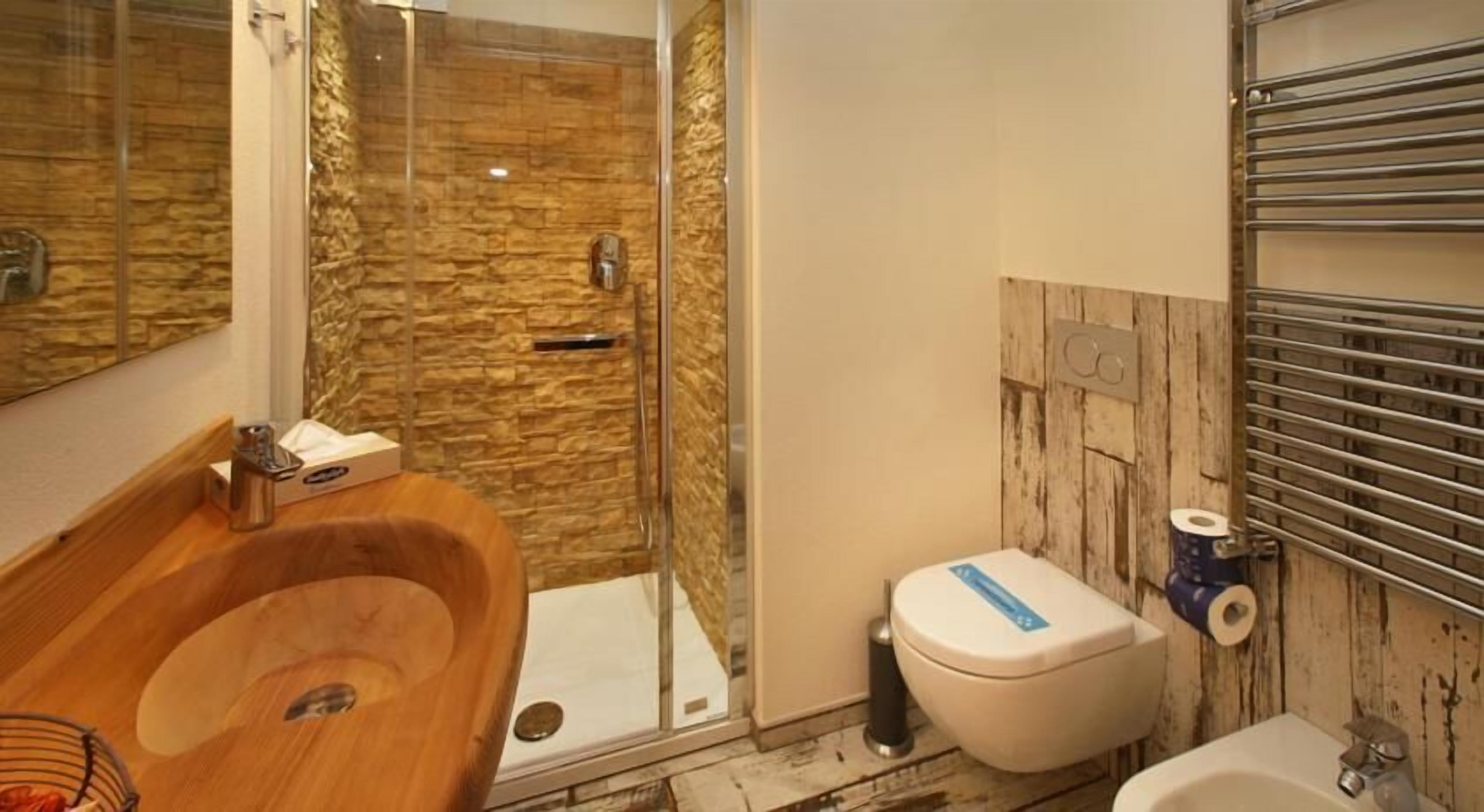 Un baño con tocador de madera, cabina de ducha de vidrio, inodoro y lavamanos.