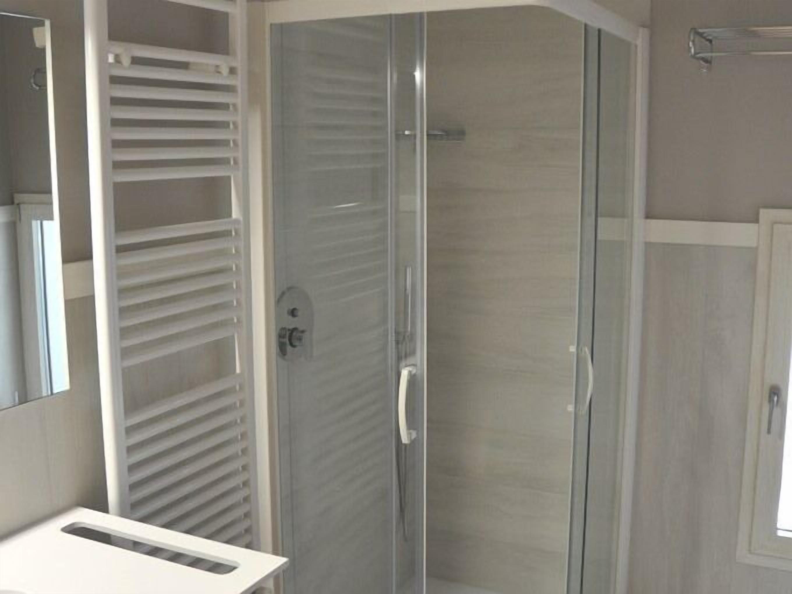 A modern bathroom with a glass shower enclosure, a white sink, and a mirror.