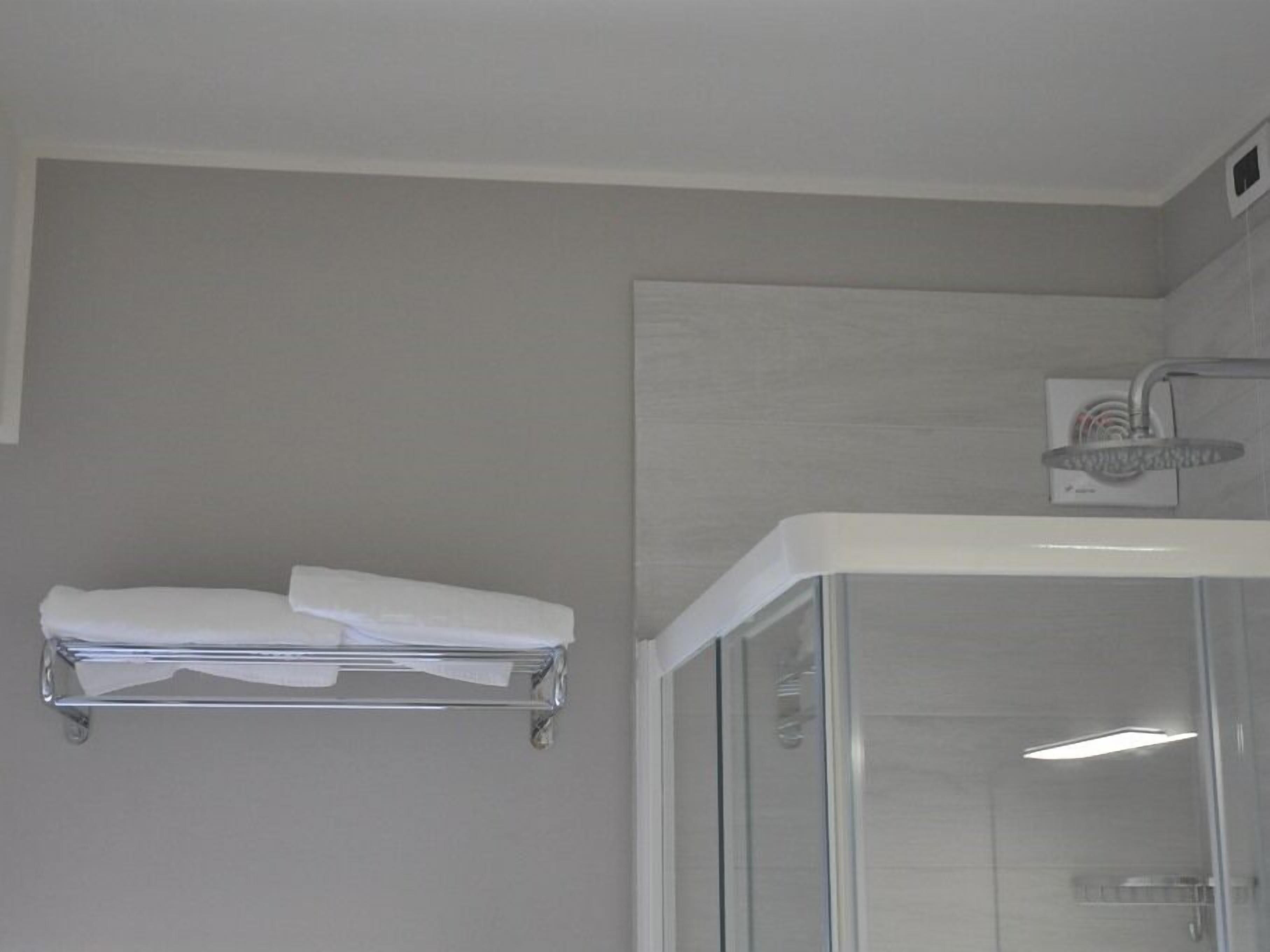 Een moderne badkamer met een douchecabine van glas, een witte handdoekhouder en een zichtbaar bedieningspaneel voor de douche.