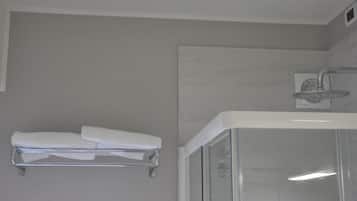 Een moderne badkamer met een douchecabine van glas, een witte handdoekhouder en een zichtbaar bedieningspaneel voor de douche.