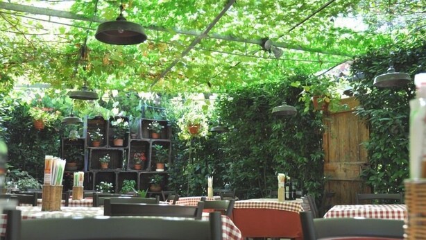 An outdoor restaurant with tables covered in checkered tablecloths, hanging pendant lights, and potted plants. - Casa Rosanna (Meolo)