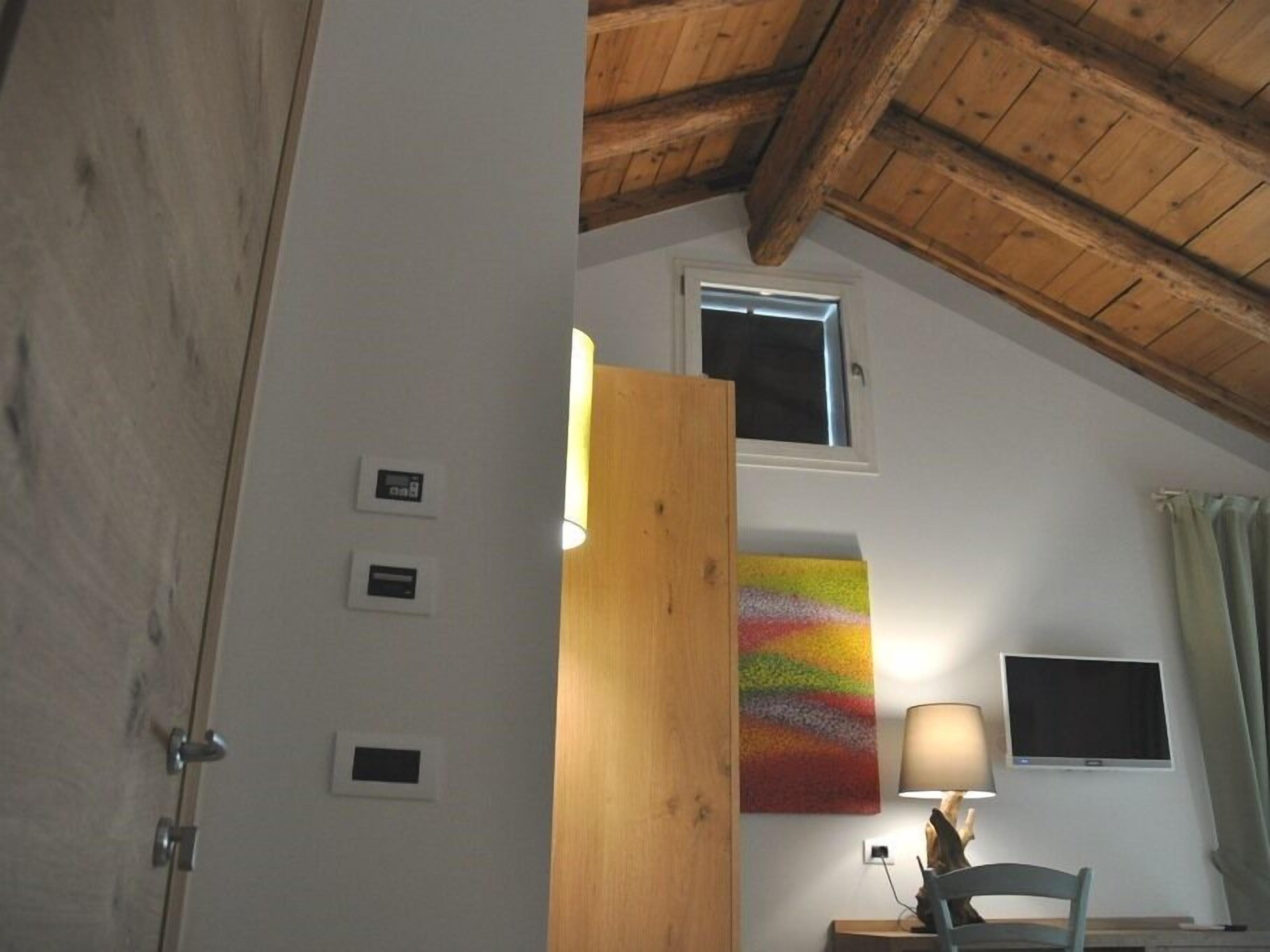Ein Zimmer mit schrägem Dach, einer Holztür, einem farbenfrohen abstrakten Gemälde, einem Fernseher und einer Lampe.