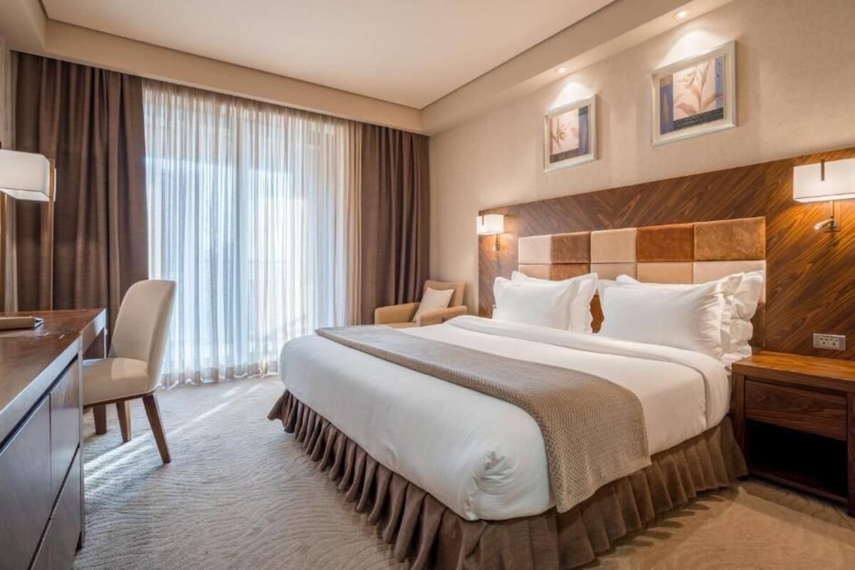 A hotel room with a large bed, a desk, a chair, and a nightstand.