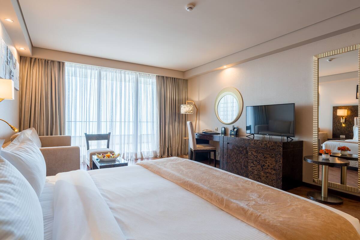 A hotel room with a large bed, a desk, a chair, a TV, and a mirror.