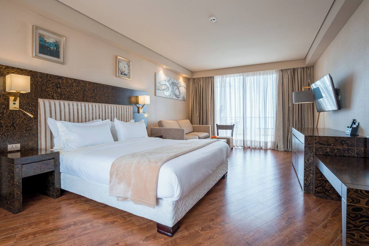 A hotel room with a large bed, a sofa, a desk, and a TV.