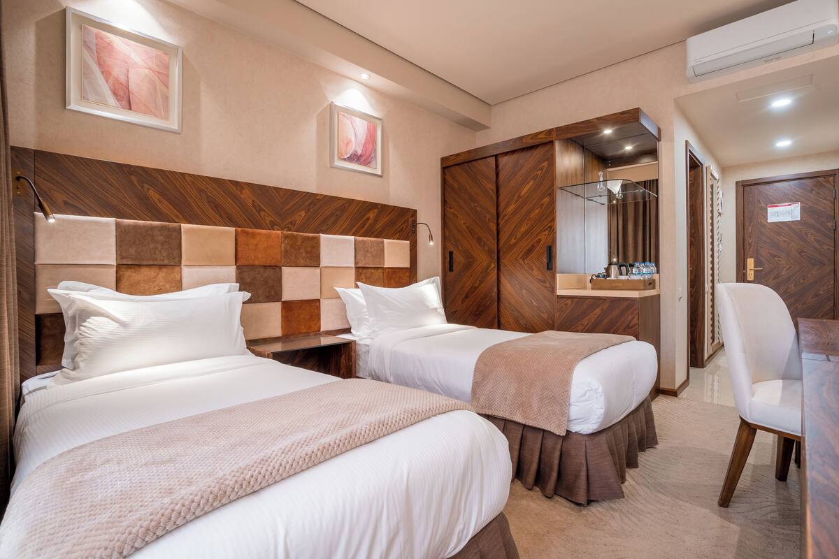 A hotel room with two beds, a wooden headboard, a desk, a chair, and a mirror.