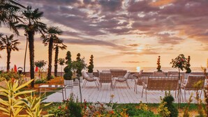 A terrace with wicker chairs and tables, palm trees, and a sunset view. - Dreamland Oasis Resort & Spa (Kobuleti)