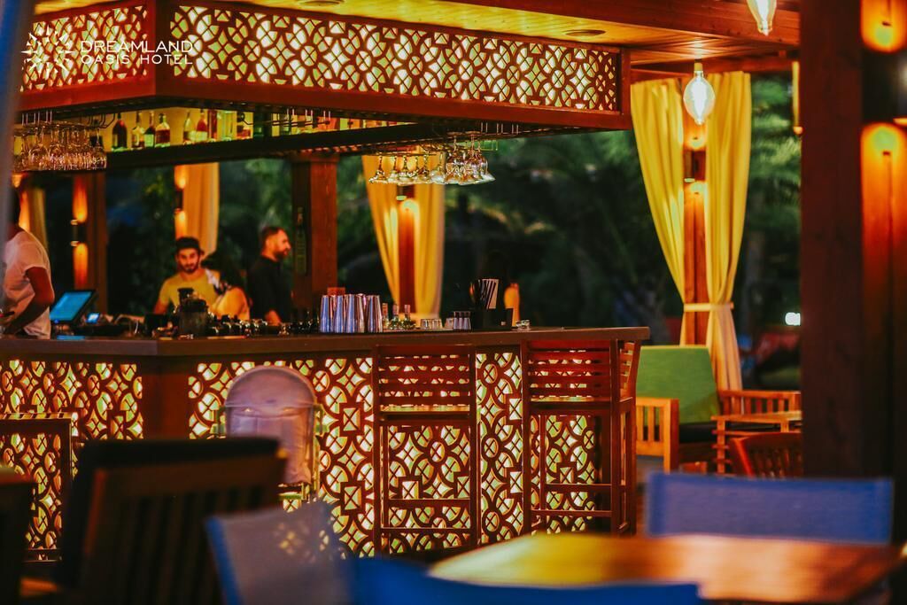 A bar area with a patterned wooden partition, bar stools, and a counter with a bartender.