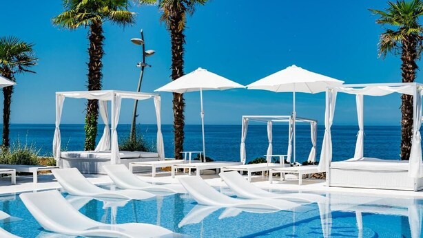 A poolside area with lounge chairs and umbrellas, palm trees, and a view of the ocean. - Dreamland Oasis Resort & Spa (Kobuleti)