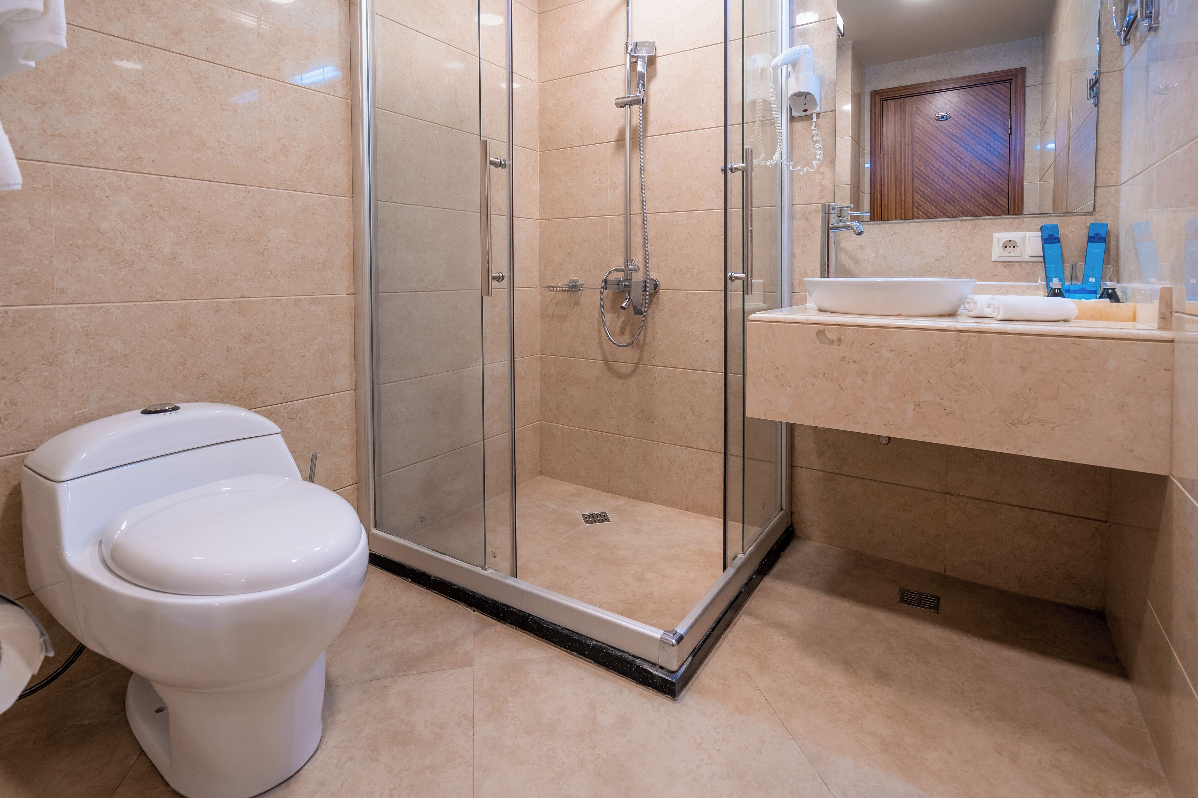 A modern bathroom with a glass-enclosed shower, a white toilet, and a sink with a mirror above.
