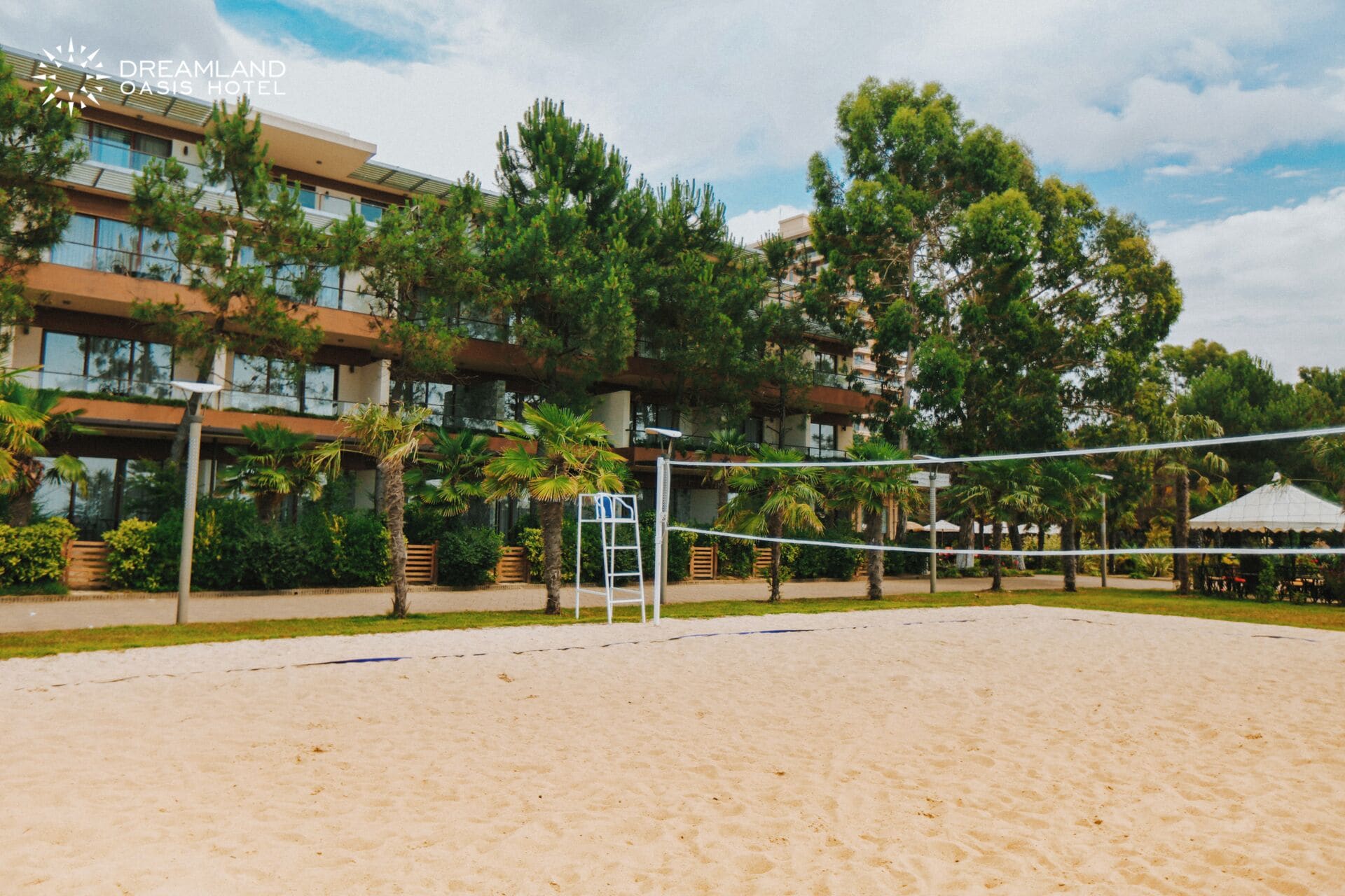 Un terrain de volleyball de plage, avec un filet, entouré d’arbres et bordé d’un bâtiment doté de balcons.