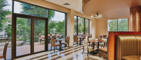 A spacious indoor area with large windows, a polished floor, and a seating area with tables and chairs.
