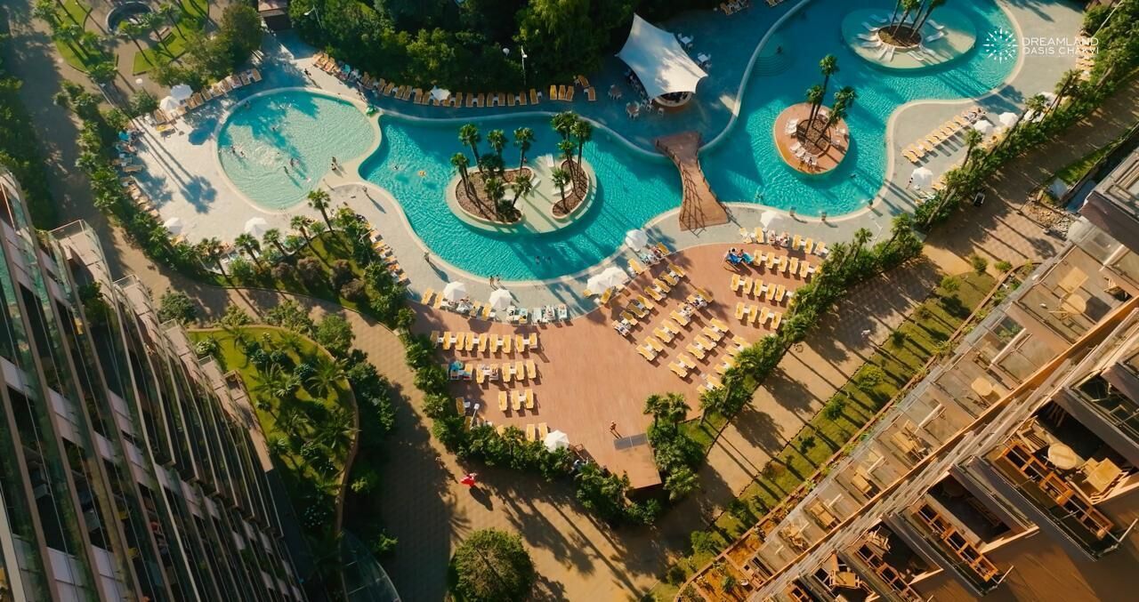 An aerial view of a resort with multiple swimming pools, sun loungers, and a central water feature.
