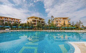Una gran piscina con sillas de descanso y sombrillas, rodeada de edificios de varios pisos con balcones.