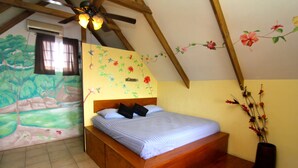 A bedroom with a wooden bed, a ceiling fan, a wall mural, and a vase with flowers. - Orange House - Over the Water Rental (Bocas del Toro)