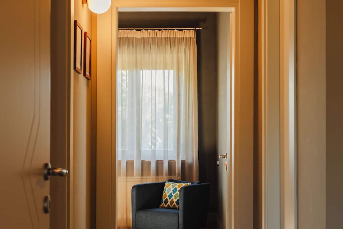 A hallway leading to a room with a window, a sofa, and a light fixture.