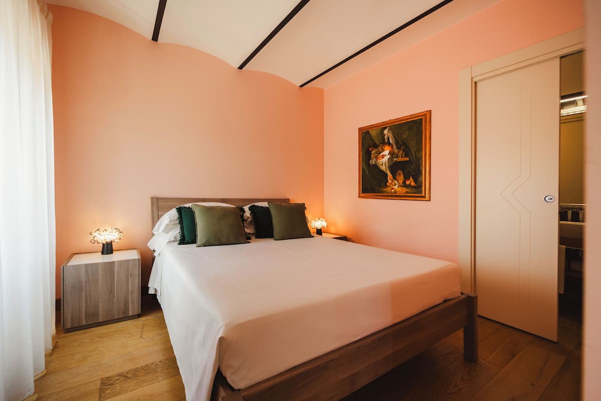 A bedroom with a bed, nightstands, a painting, and a wardrobe.