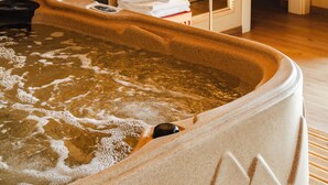 A hot tub with a textured exterior, a towel stack, and a floor lamp in a room with wooden flooring and a marble wall.