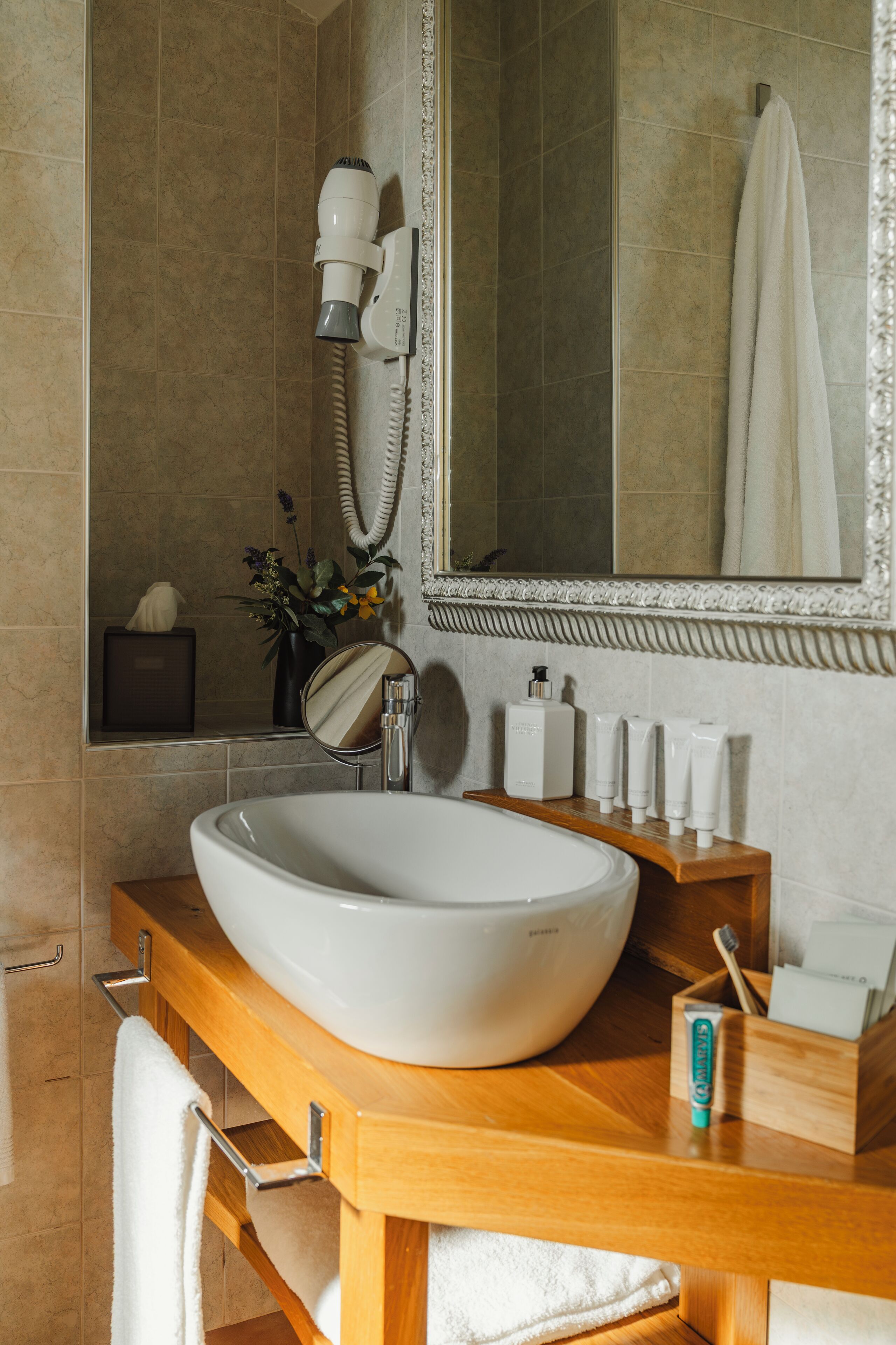 A bathroom with a large white sink, a mirror, a hairdryer, and toiletries on the counter.