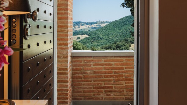 A doorway leading to a balcony with a view of a hilly landscape.