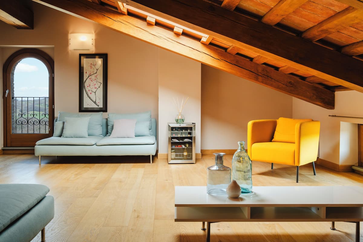 A spacious loft with a wooden ceiling, a light blue sofa, a yellow armchair, and a small table with decorative items.