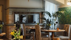 A cozy dining area with a round wooden table, rustic chairs, and a brick fireplace.