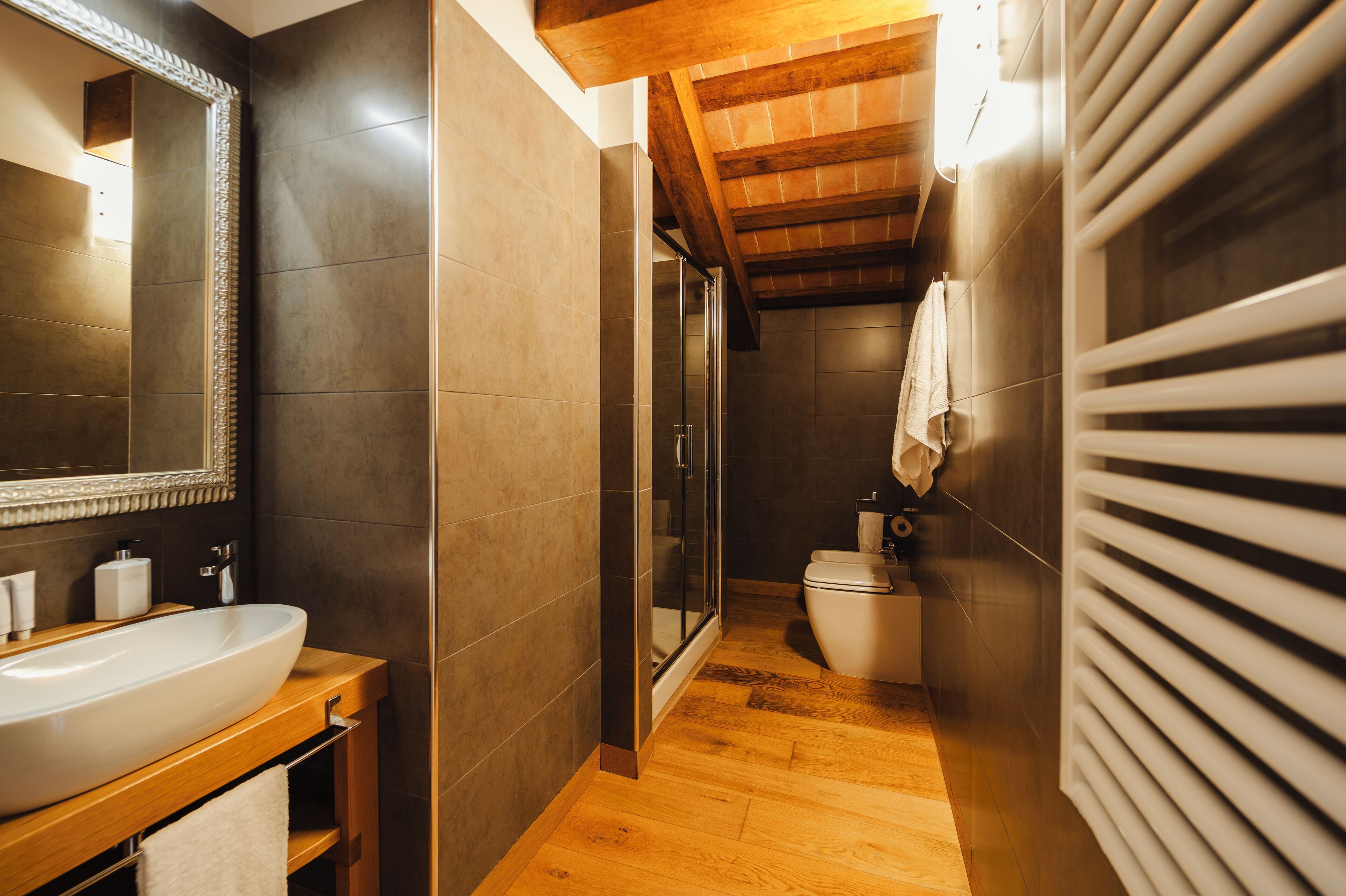Een moderne badkamer met een grote spiegel, een houten wastafelmeubel, een glazen douchecabine en een wit toilet.