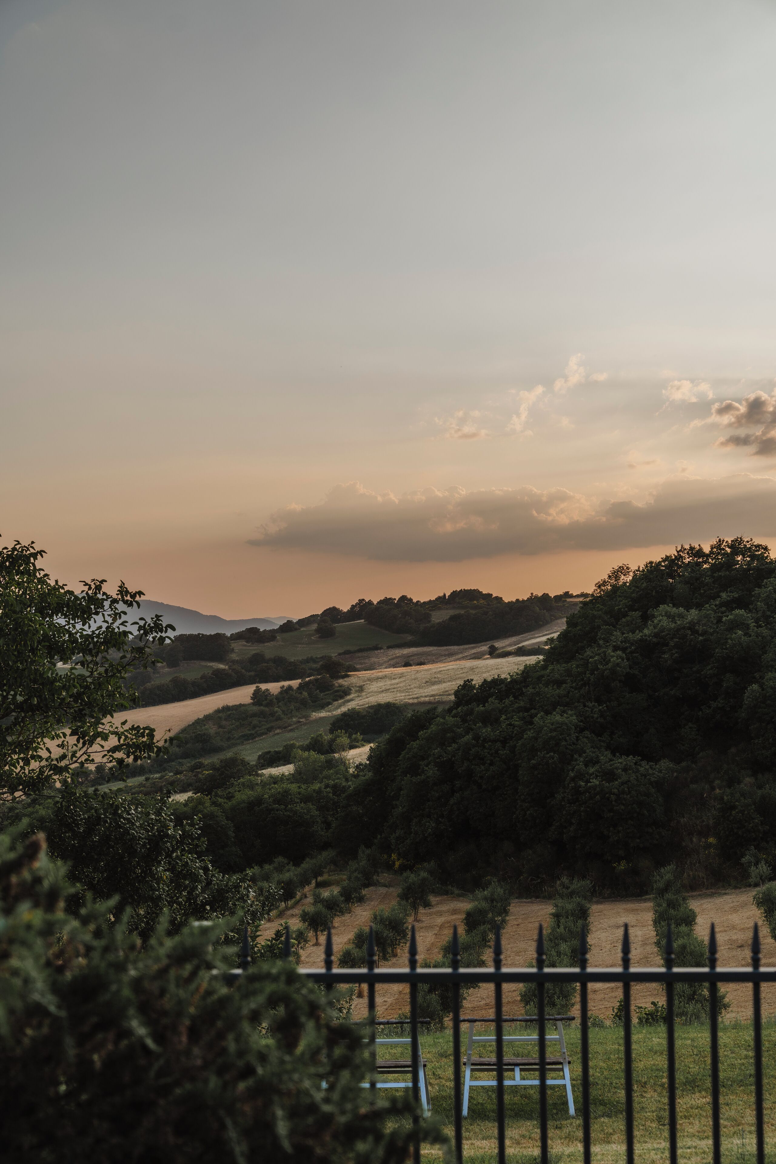 A rural landscape with rolling hills, a river, and a fence with a bench.