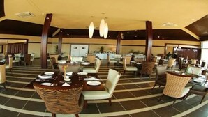 A spacious indoor dining area with multiple tables and chairs, a central decorative bowl, and a high ceiling with hanging lights. - Rlj Kendeja Resort and Villas (Monrovia)