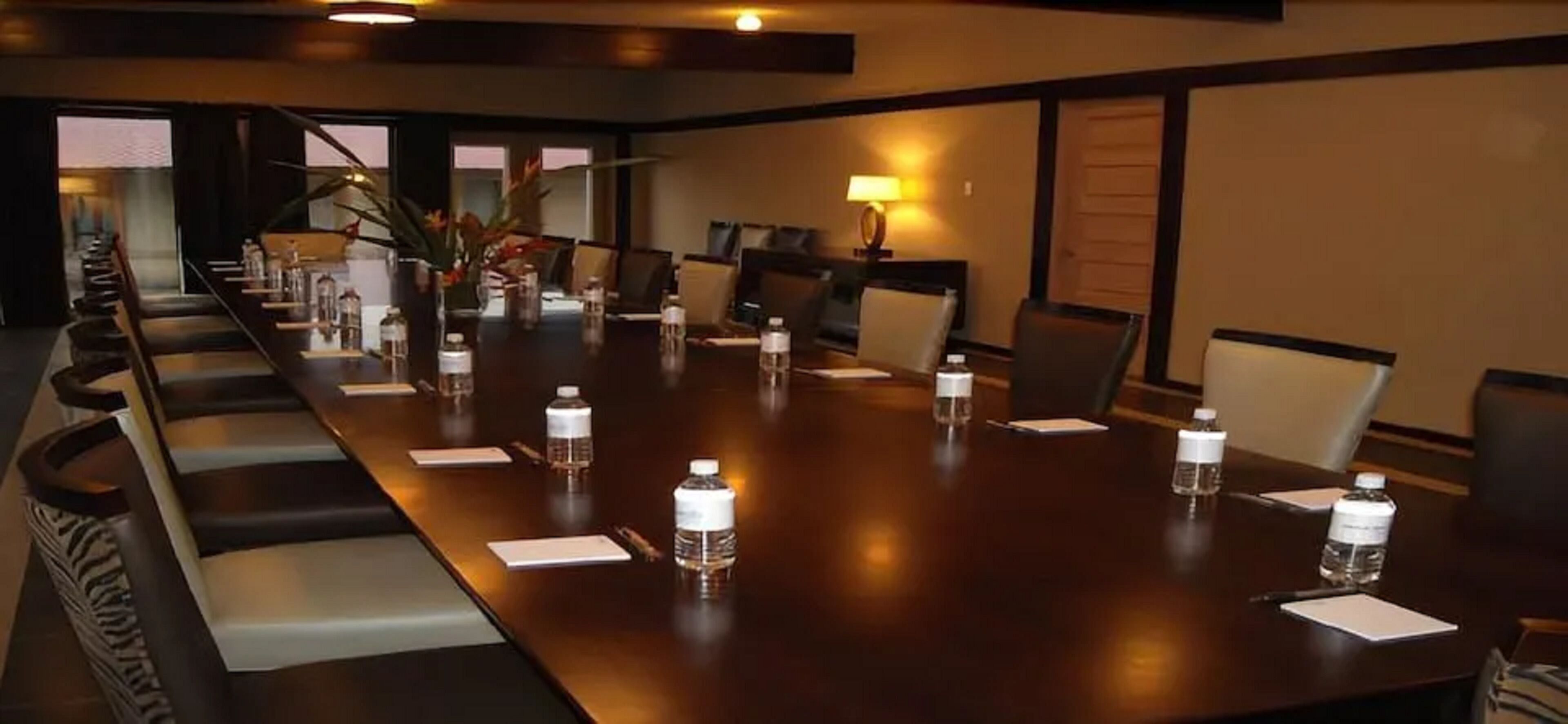 Uma sala de conferência com uma mesa comprida, cadeiras, garrafas de água e um abajur.
