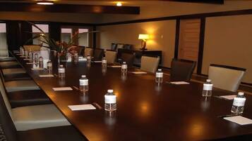 Uma sala de conferência com uma mesa comprida, cadeiras, garrafas de água e um abajur.