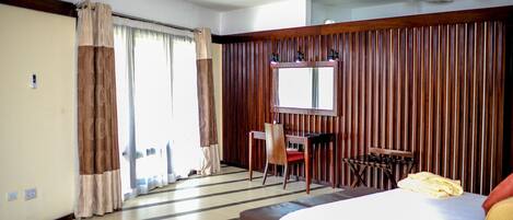 Una habitación de hotel con cama, escritorio, silla, espejo y ventilador de techo.