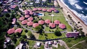An aerial view of a resort with multiple red-roofed buildings, a central swimming pool, and a beachfront. - Rlj Kendeja Resort and Villas (Monrovia)