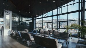 Un amplio salón con muebles modernos, ventanas grandes con vistas a la ciudad y una escalera que sube a niveles superiores.