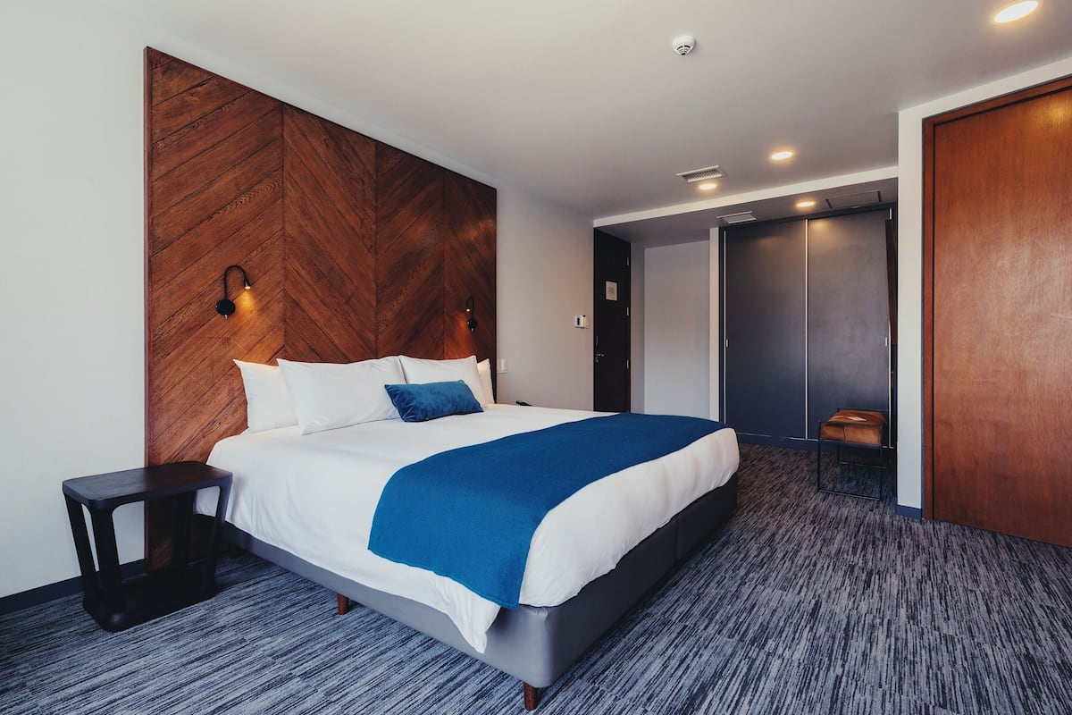 A modern hotel room with a large bed, a wooden accent wall, and a separate seating area.